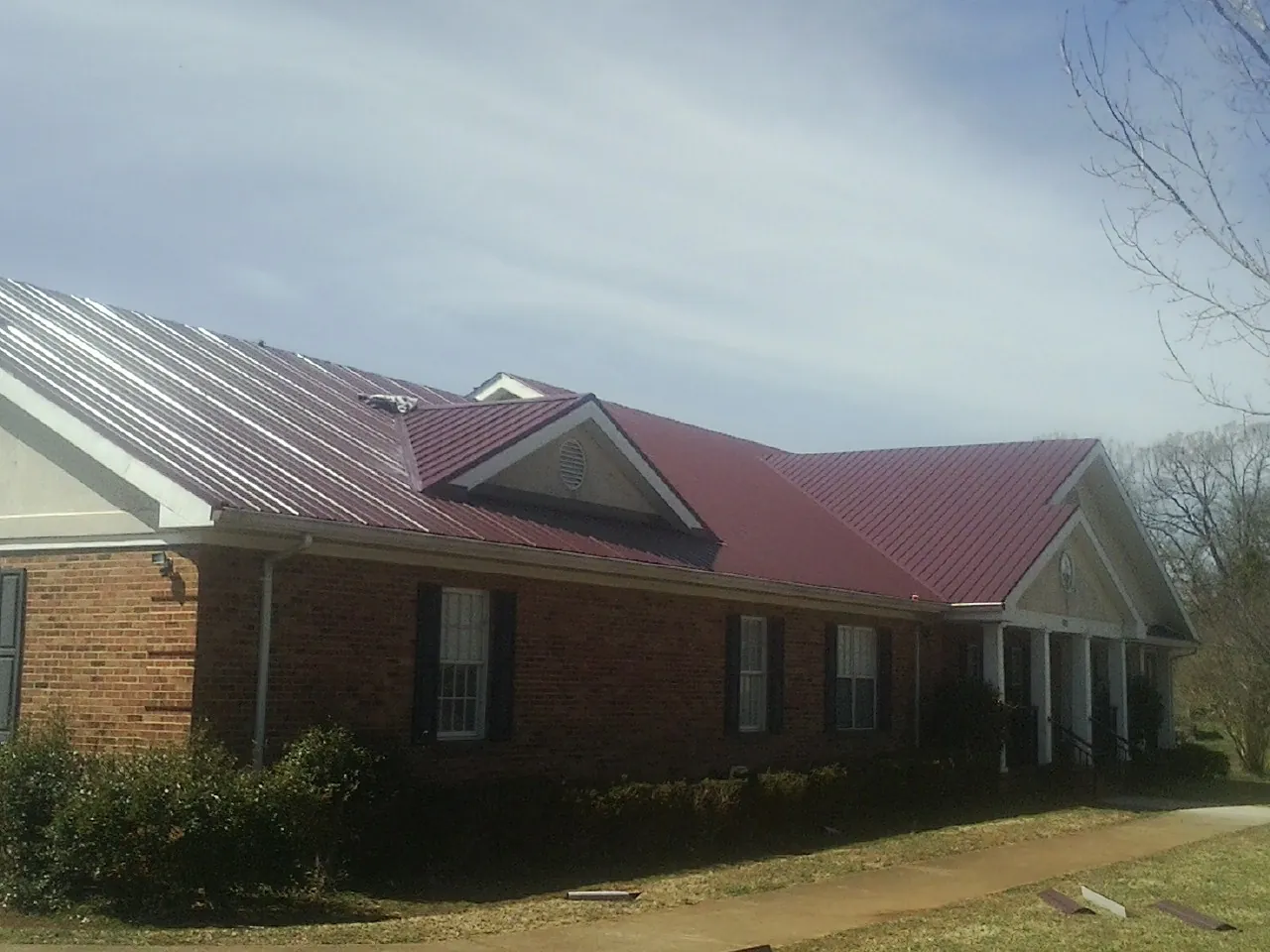 Red metal roof with gabled entries on a long brick building, from a Hail Damage Roof Repair job in Fort Dodge