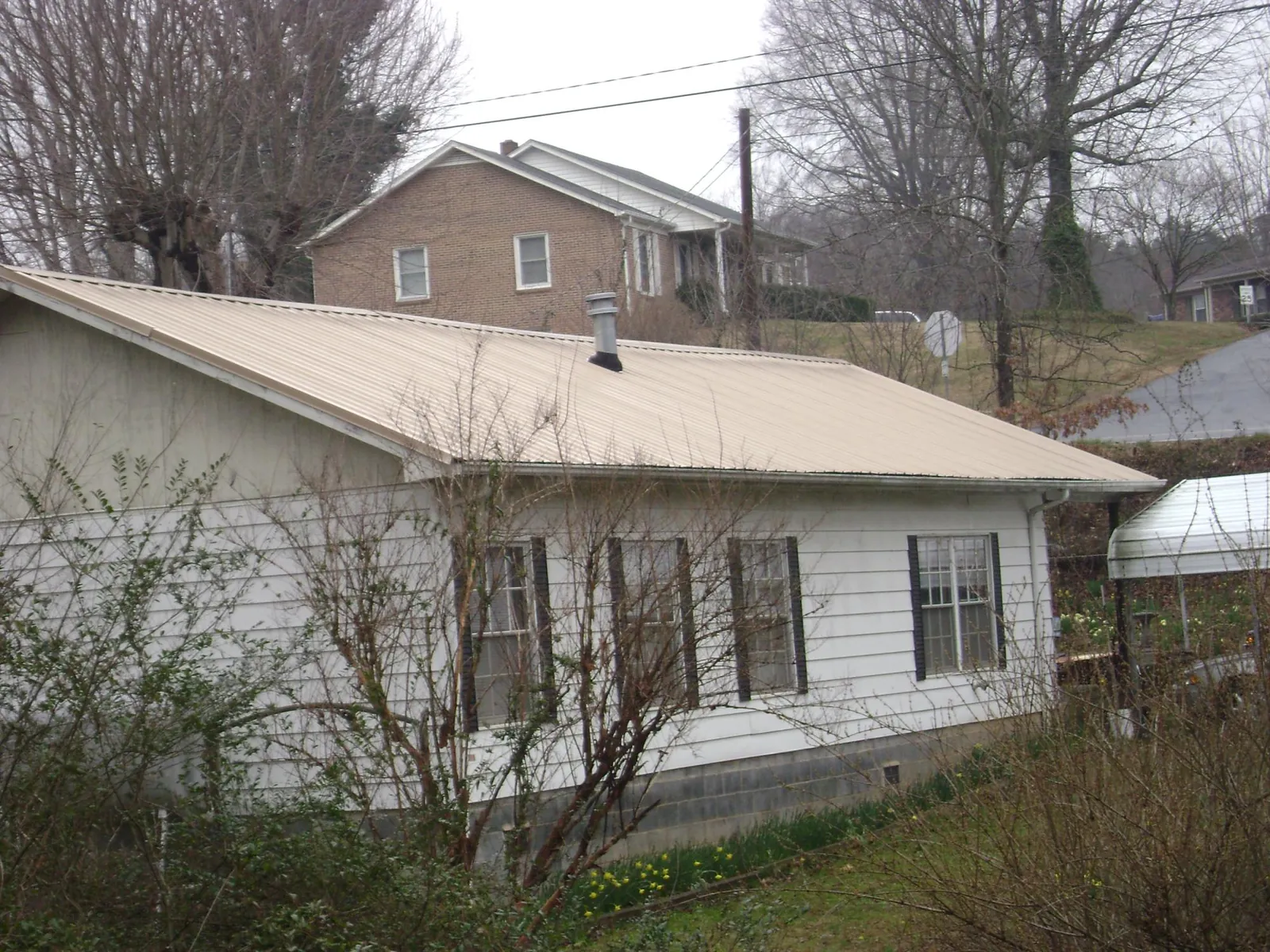 Tan metal roof on a white sided house set into a hillside — Commercial Roofing by Roofing Brothers in Fort Dodge